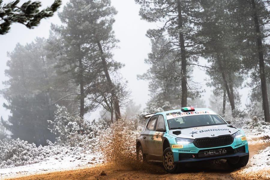 Vettura da rally nella neve fra i pini, avvolta dalla nebbia